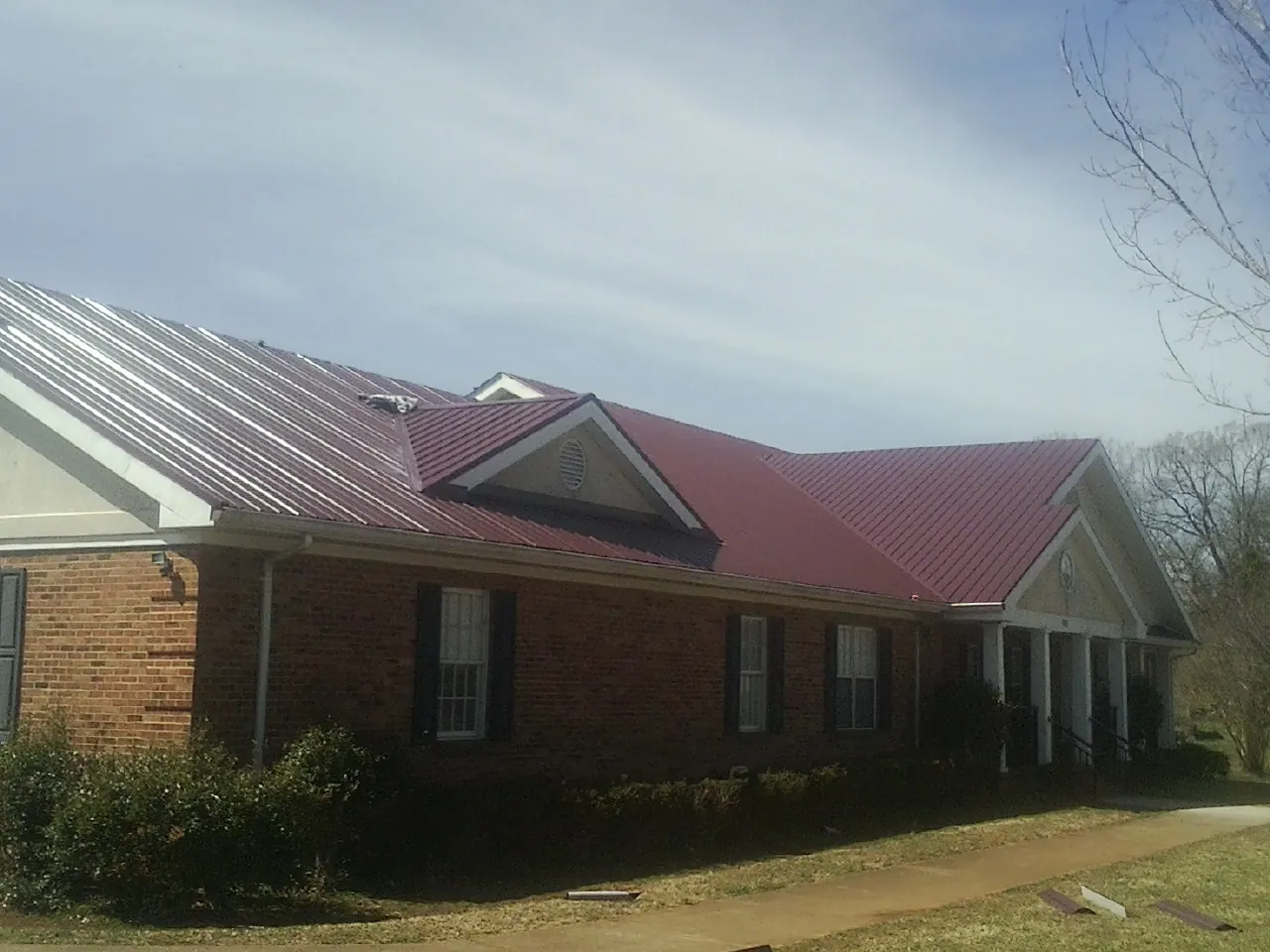 Red metal roof with gabled entries on a long brick building, from a Hail Damage Roof Repair job in Laporte