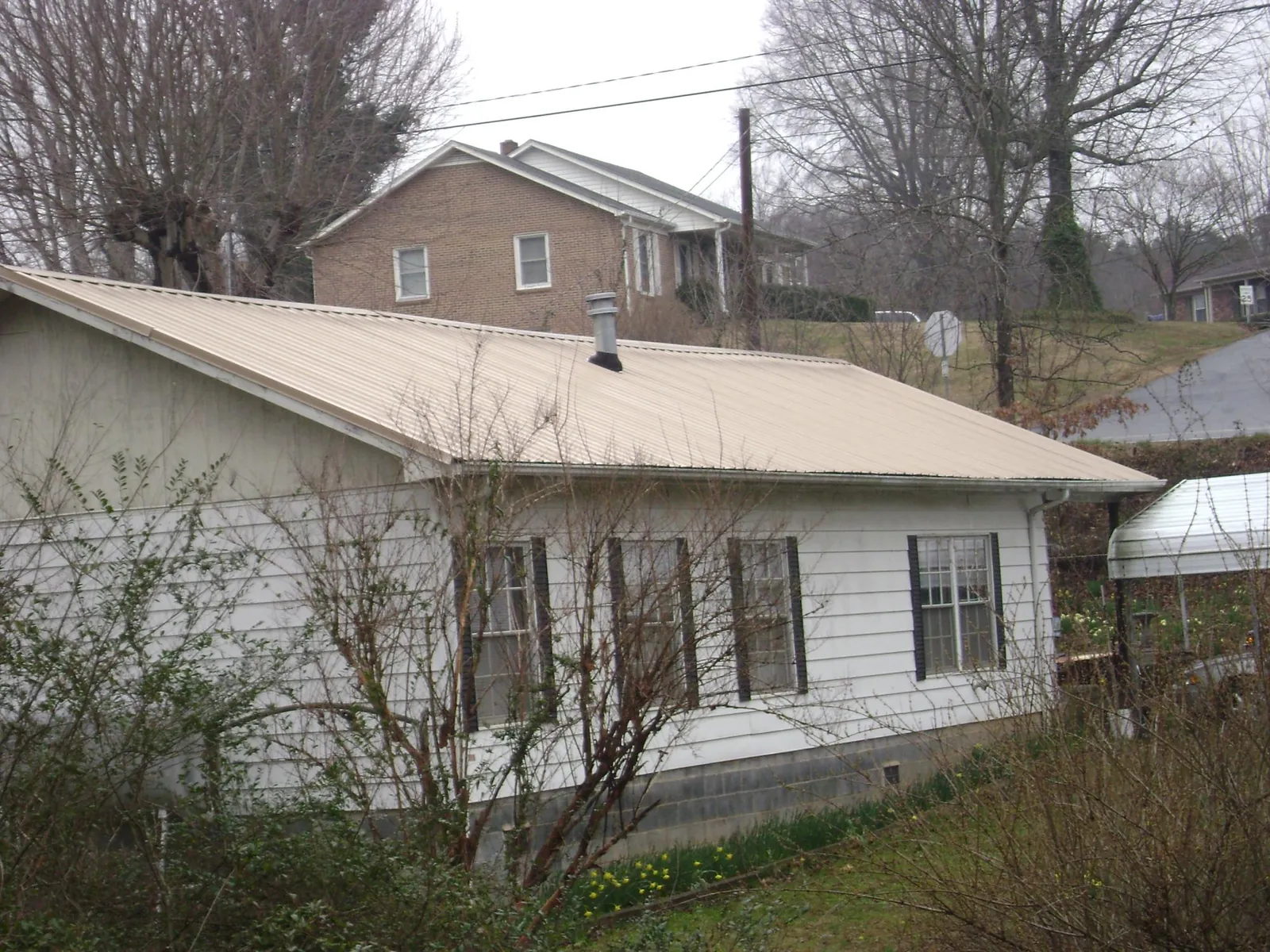 Tan metal roof on a white sided house set into a hillside — Commercial Roofing by Roofing Brothers in Laporte