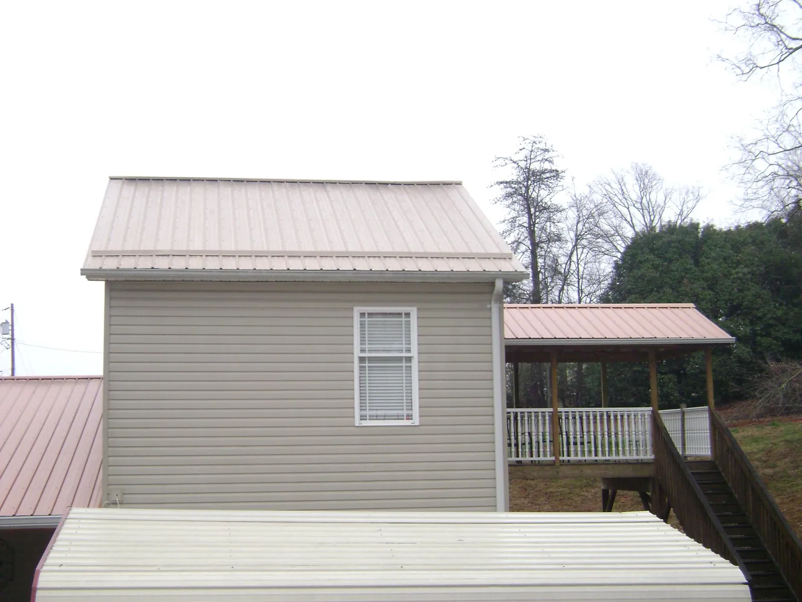 Tan metal roofs on a two story addition and attached porch, from a Roof Replacement job in Laporte